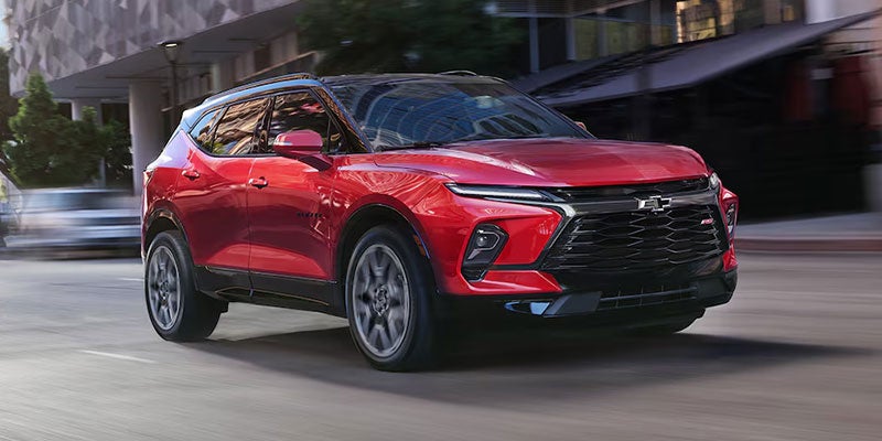 Red Chevrolet Blazer SUV driving through an urban street, featuring a bold black grille