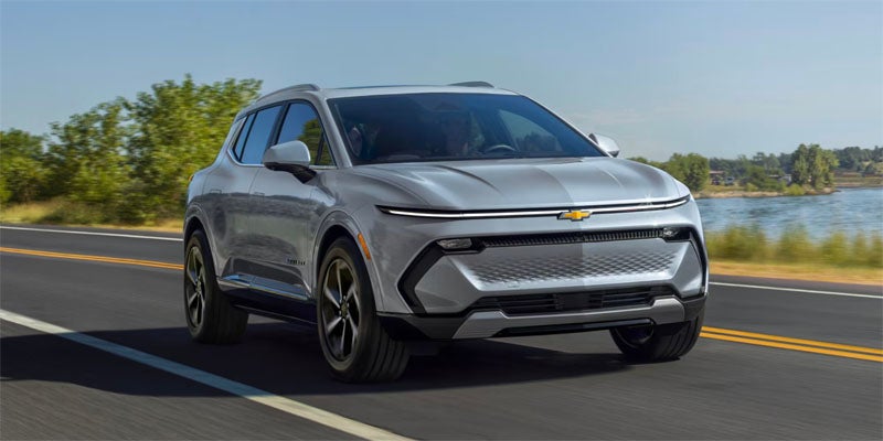 Silver Chevrolet Equinox EV driving on a paved road near a lake