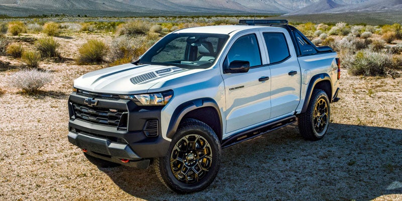 White Chevrolet Colorado off-road pickup truck parked on a desert trail with rugged terrain and mountains in the background