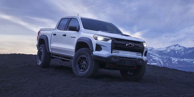 White Chevrolet Colorado ZR2 off-road pickup truck on a rocky mountain landscape under a cloudy sky