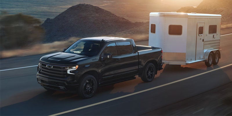 Black Chevrolet Silverado 1500 towing a white horse trailer on a highway