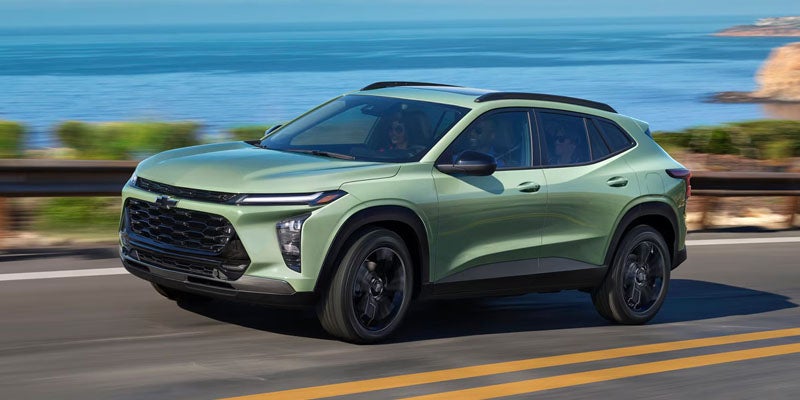 Light green Chevrolet SUV driving on a coastal highway with ocean views, roadside barriers, and rocky cliffs in the background