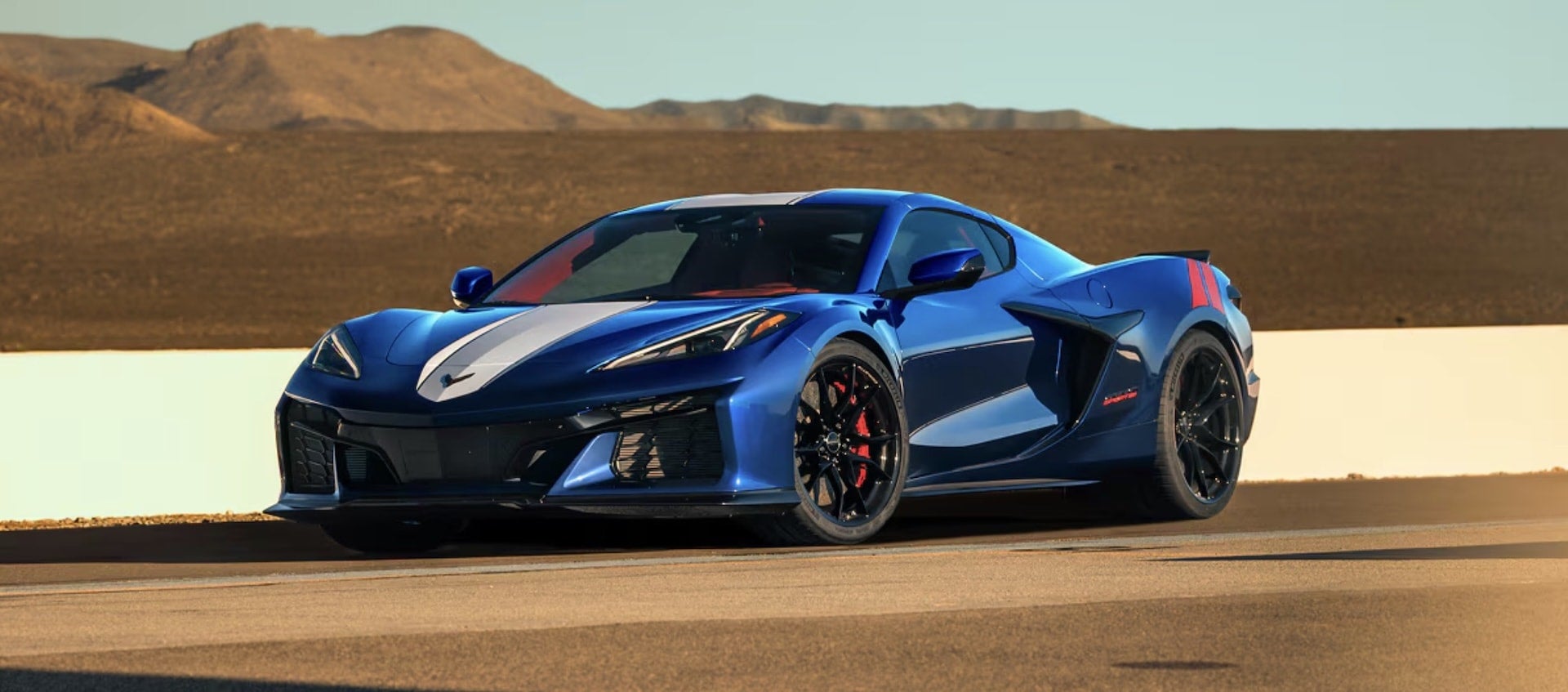 2027 Chevrolet Corvette Grand Sport in blue, front three-quarter view with white hood stripes and red brake calipers