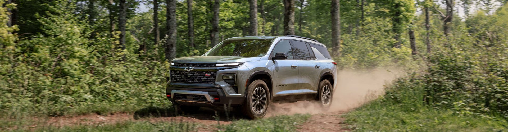 2026 Chevrolet Traverse driving on a dirt road through a forest