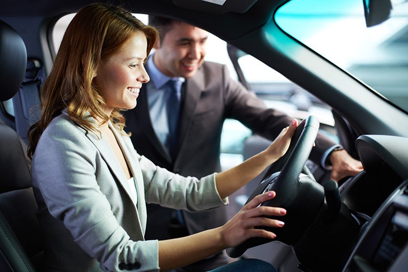 Smiling woman sitting in driver's seat with salesman at a dealership