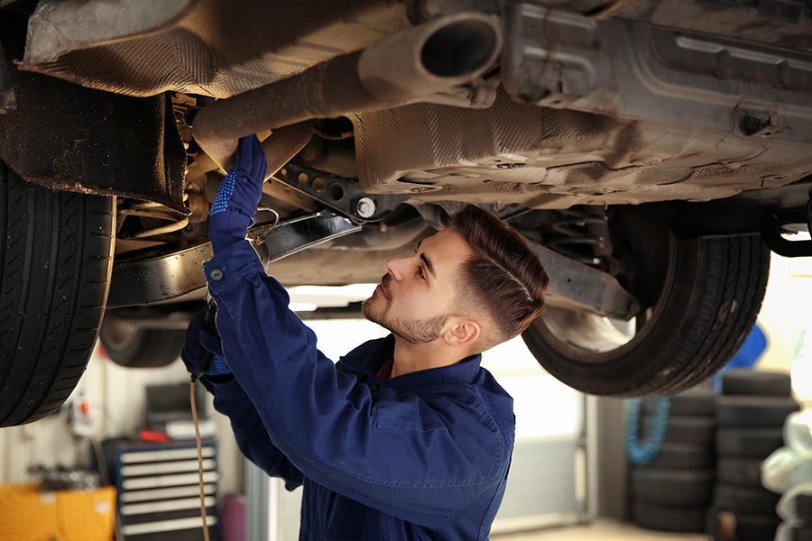 Mechanic in blue uniform inspecting the undercarriage of a car